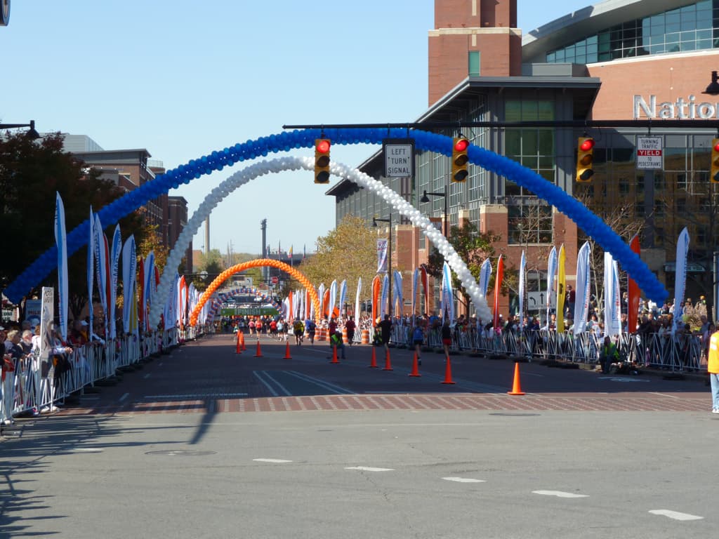 Blue, white, and orange balloon arches above the 2010 Columbus Marathon finish corridor, with spectators behind barriers.